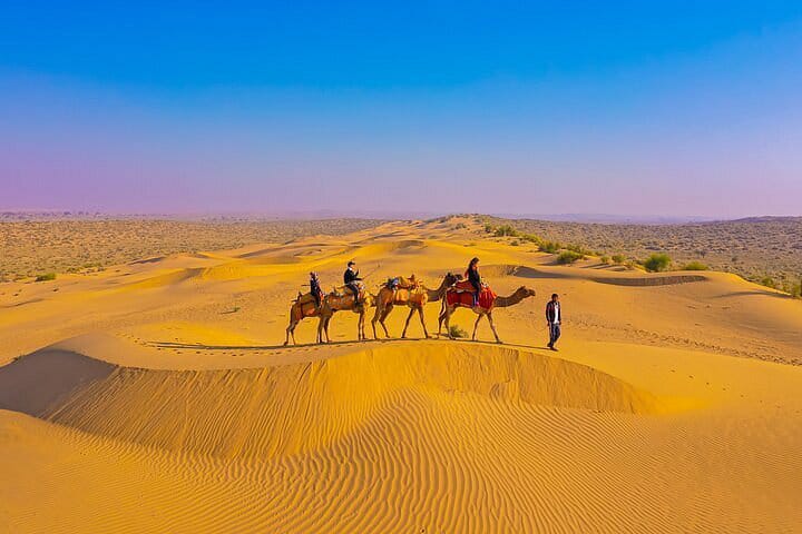Camel safari riders crossing golden desert dunes at sunset